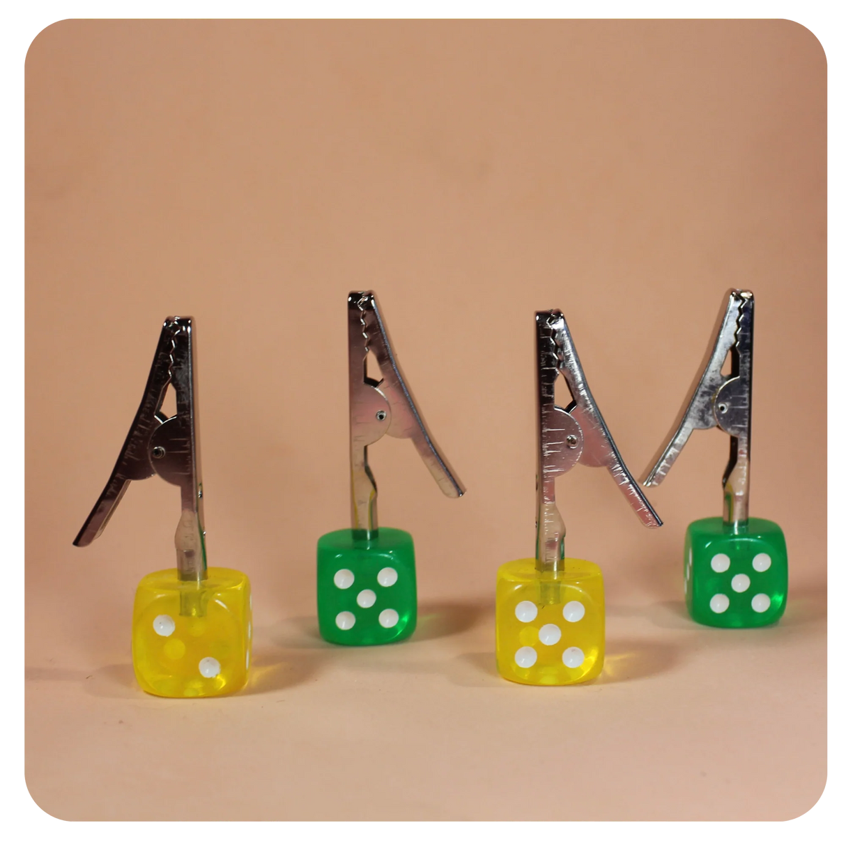 Front angled view of the Dice Roach Clip 10 Piece Pack in yellow and green. Featuring a sturdy metal alligator clip topped with a classic casino-style die, these helpful smoking accessories securely hold joints to prevent burned fingers.