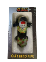 Angled profile view of the 5" Glizzy Clay Hand Pipe with a green accent. This novelty food-themed clay smoking instrument is designed to visually replicate a hot dog, featuring an integrated deep-dish bowl and side-carb.