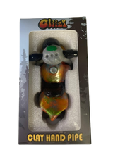 Angled profile view of the 5" Glizzy Clay Hand Pipe with a red accent. This novelty food-themed clay smoking instrument is designed to visually replicate a hot dog, featuring an integrated deep-dish bowl and side-carb.