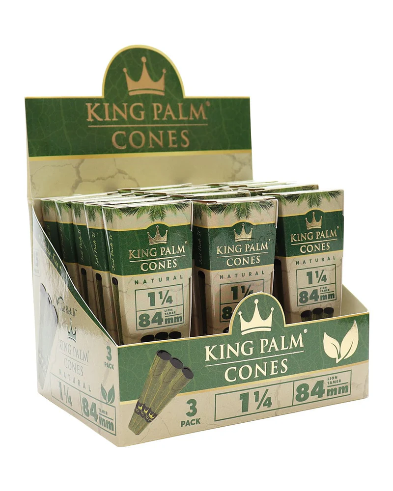 Front angled view of the King Palm Natural Cones 1 1/4 Size 84mm 15-count display carton in green and gold packaging. These fully formed, tobacco-free Cordia leaf wraps feature a pre-installed paper filter and arrive ready to pack with unrefined botanical materials.