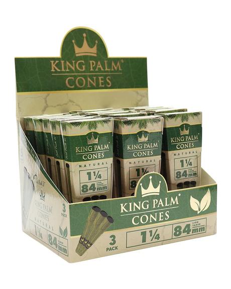 Front angled view of the King Palm Natural Cones 1 1/4 Size 84mm 15-count display carton in green and gold packaging. These fully formed, tobacco-free Cordia leaf wraps feature a pre-installed paper filter and arrive ready to pack with unrefined botanical materials.