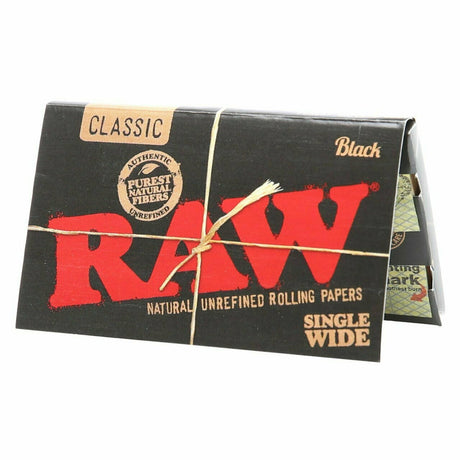 Front flat lay view of a single RAW Classic Black Single Wide booklet in black with gold lettering. Each compact booklet contains ultra-thin, unbleached rolling papers designed to burn slowly and perfectly preserve the natural flavor of your dry herb.