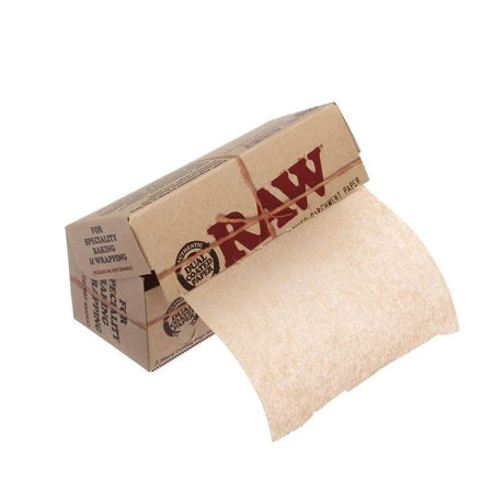 Front angled view of the RAW Dual Coated Parchment Paper Roll box in natural kraft brown packaging with green and red branding. Measuring a compact 10cm wide by 4m long, this unrefined, extra-slick parchment paper is specifically designed for safely handling and storing sticky botanical extracts on the go.