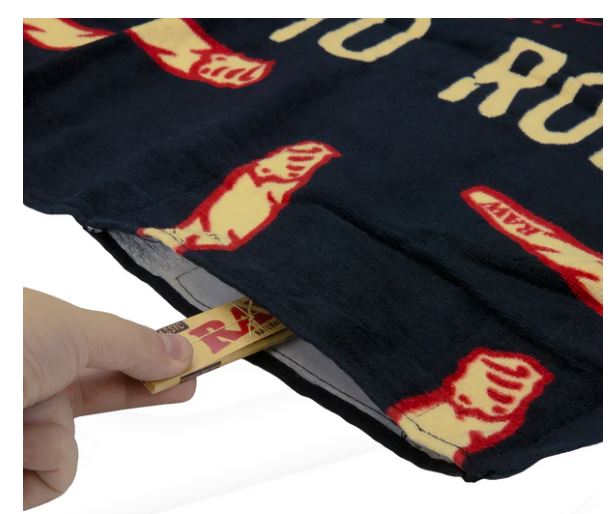 Close-up view of the RAW Stash Pocket Beach Towel in black and red, highlighting the concealed compartment. This 100% cotton large-format fabric features an integrated Velcro-sealed stash pocket to safely conceal smoking hardware and unrefined materials from the elements.