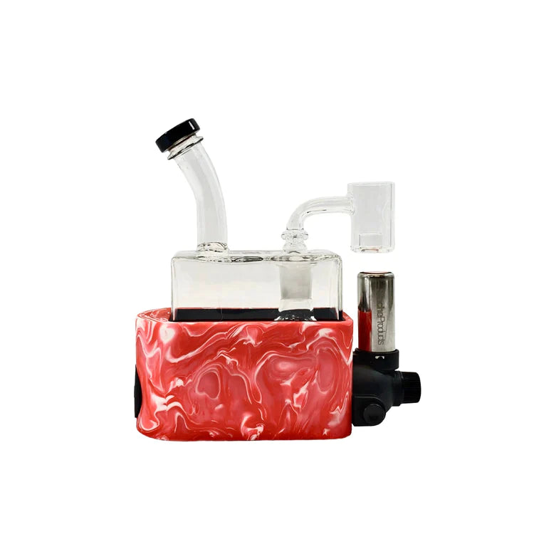 Front view of the Stache Rig in One mechanical dab rig with a pink silicone base sleeve. This all-in-one setup integrates a refillable butane torch directly below a quartz banger for convenient, cordless concentrate dabbing.