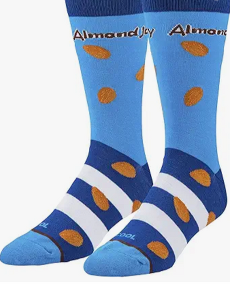 Front view of a pair of Crazy Socks featuring officially licensed Almond Joy graphics. These vibrant novelty crew socks showcase the classic white and red candy logo alongside detailed almond and coconut graphics against a rich royal blue background.