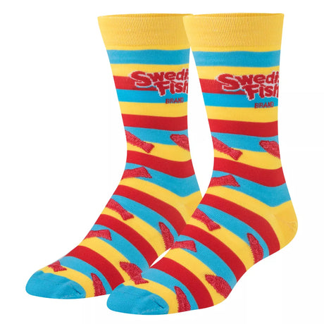 Front view of a pair of Crazy Socks featuring officially licensed Swedish Fish graphics. These colorful novelty crew socks display rows of iconic red fish swimming across bold yellow, red, and blue candy stripes to add a playful pop to your daily outfit.