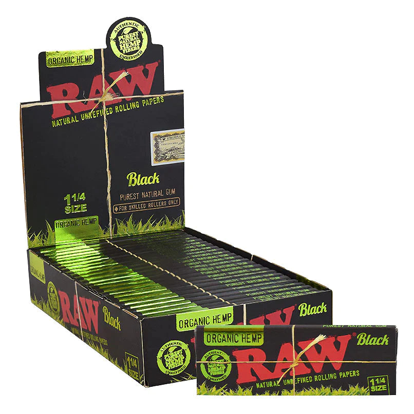 Front angled view of the RAW Black Organic Hemp Paper 1 1/4 24-count display box in matte black and tan packaging with green branding. This retail-ready counter carton neatly showcases these double-pressed, ultra-thin organic hemp rolling papers for quick point-of-sale customer impulse buys.
