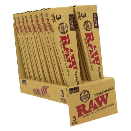 Front angled view of the RAW Classic Peacemaker Cones 16-count display box in natural kraft brown packaging with red branding. Made from unrefined, unbleached plant fibers, these retail-ready boxes hold 140mm pre-rolled cones designed for extended group sessions.