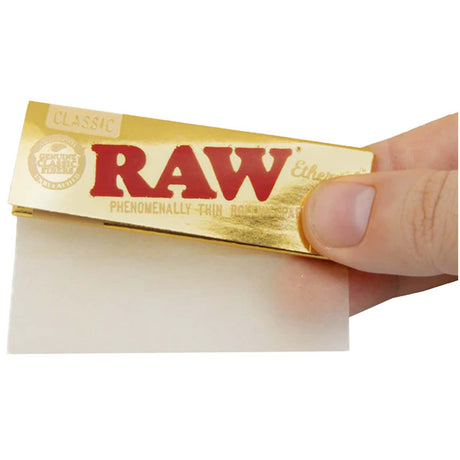Front view of the RAW Ethereal 1 1/4 size rolling papers in a 24-count gold and black retail display box. These low-density, ultra-thin papers feature a clean tree sap adhesive and are engineered to minimize the taste of paper ash.