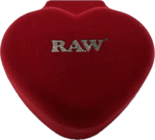 Angled overhead view of the closed red velvet heart-shaped jewelry box featuring an embossed gold RAW logo on the lid. This luxury protective case keeps your delicate borosilicate glass smoke stone safe and pristine between desktop sessions.