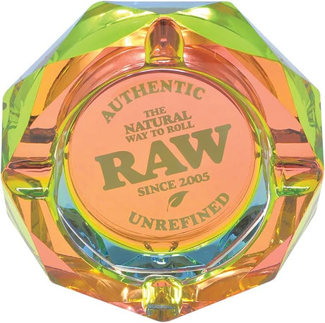 Angled top-down view of the RAW Rainbow Geometric Glass Ashtray showcasing its multi-faceted crystalline shape. This heavy-duty prismatic glass ashtray flashes a spectrum of iridescent rainbow colors and features the iconic red RAW logo centered in the ash basin.