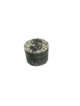 Angled overhead view of the Smoke Zilla Magnetic Grinder featuring a melting money decal. The built-in magnetic center post ensures the lid stays firmly attached to the grinding chamber while in pockets or bags.