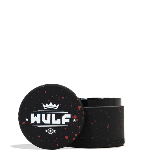 Front angled view of the Wulf 4-Piece 65mm Aerospace Aluminum Grinder in black with red splatter. Crafted from durable aerospace-grade metal, this large multi-chamber grinder effortlessly shreds dry botanicals to the perfect consistency for rolling or packing.