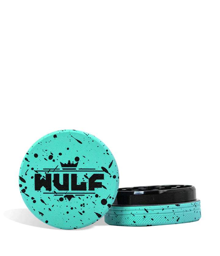Front angled view of the Wulf Mods 2-Piece 65mm Spatter Aluminum Grinder in teal with black paint splatter. This compact, travel-friendly magnetic herb grinder features a streamlined two-piece design to quickly and efficiently shred your botanical blends without added bulk.