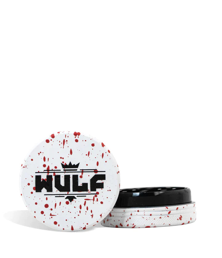 Front angled view of the Wulf Mods 2-Piece 65mm Spatter Aluminum Grinder in white with vibrant red paint splatter. This compact, travel-friendly magnetic herb grinder features a streamlined two-piece design to quickly and efficiently shred your botanical blends without added bulk.